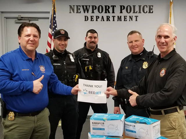 Five members of the Newport Police Department pose with boxes of N95 masks and a sign that says