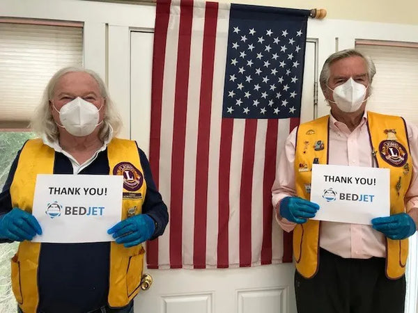 Two members of the Newport Lions Club pose on either side of an American Flag holding signs that say