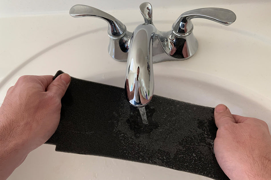 a person rinsing a BedJet air filter under running water in the sink to clean it